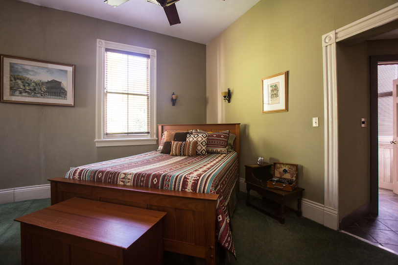 A wide-angle view of a guest room with a bed, nightstand, and window.