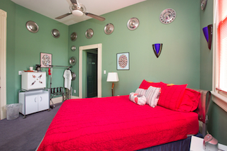 A wide-angle view of a guest room with a red bed, green walls, and decorative plates.