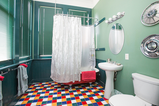 A bathroom with a colorful tiled floor, a shower with a clear curtain, a white sink, and a toilet.