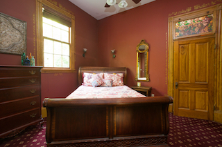 A wide view of a guest room with a wooden bed, dresser, and window