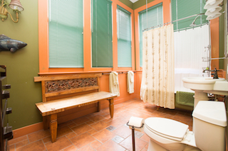 A bathroom with a toilet, sink, shower, and bench.