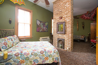 A colorful guest room with a bed, fireplace, and artwork.